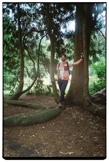 Leaning on a big tree in the woods, holding a bottle